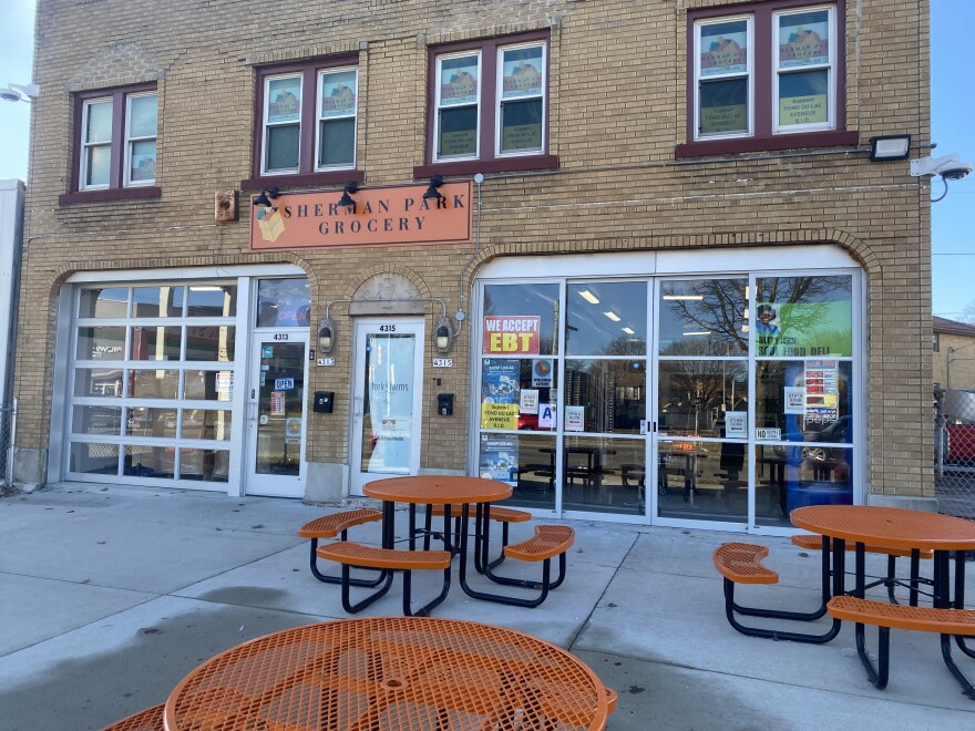 The exterior of the Sherman Park Grocery Store features several round orange lunch tables on its patio.