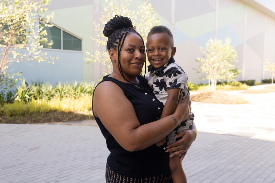 A woman smiles at the camera while holding her young son 