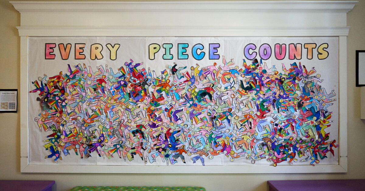 Image shows a bulletin board with the message: "Every piece counts" and artwork displaying dozens of hand-colored paper figures of children of different races.