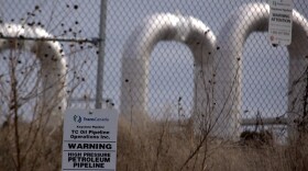 A sign for TC Energy on a fence with pieces of pipeline in the background. 