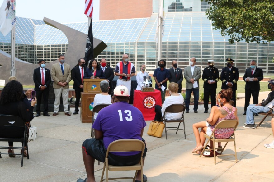 Mayor Rita Ali speaking at the ceremony with city officials alongside her.