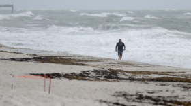 A beach goer walks along the shore as waves churned up by Tropical Storm Isaias crash near Jaycee Beach Park, Sunday, Aug. 2, 2020, in Vero Beach, Fla. Isaias weakened from a hurricane to a tropical storm late Saturday afternoon, but was still expected to bring heavy rain and flooding as it barrels toward Florida. (AP Photo/Wilfredo Lee)