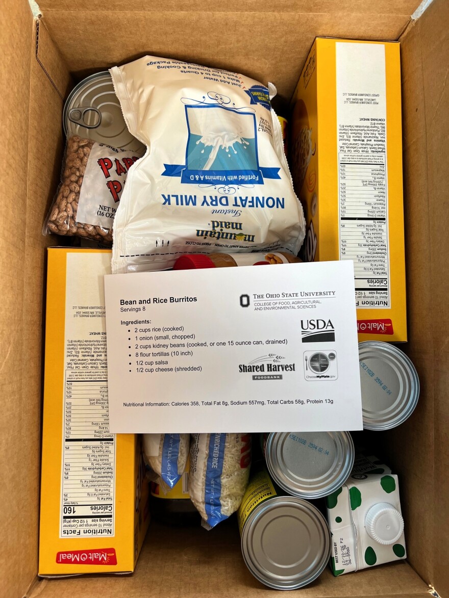 Inside a cardboard box, there are boxes of cereal, cartons of juice and bags of rice and dry beans. A recipe for burritos sits on top of the food.