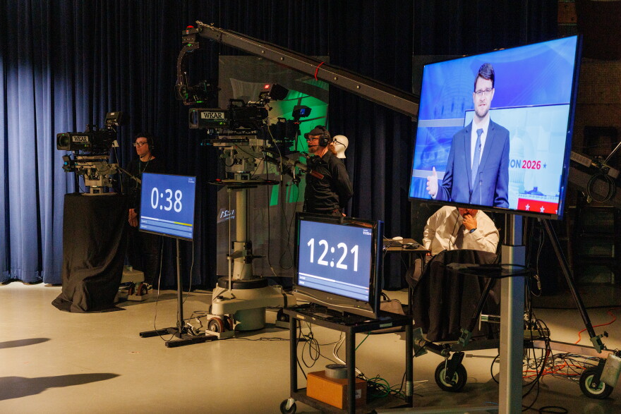 Democratic nominee for U.S. House William Lawrence is seen on a television in WKAR's studios in East Lansing, Mich., as he speaks during the first debate with U.S. Rep. Tom Barrett, R-Charlotte, on Oct. 6, 2026.