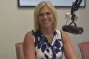 Woman in radio studio wearing flower-patterned blue and white sleeveless top and seated next to a microphone 