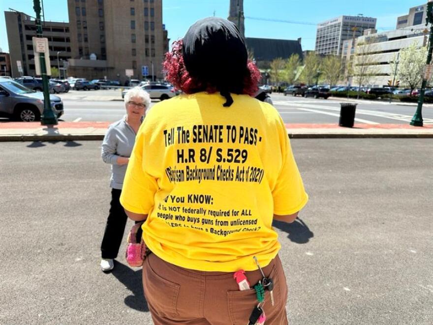 The back of a yellow shirt that says to pass the Universal Background Checks Act.