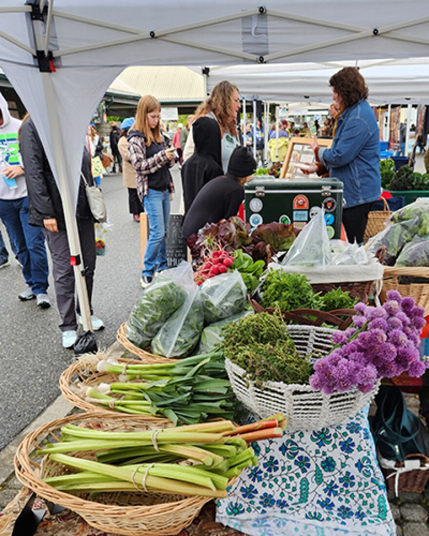 Various fruits and vegetables lay in baskets on tables as people look through them.  