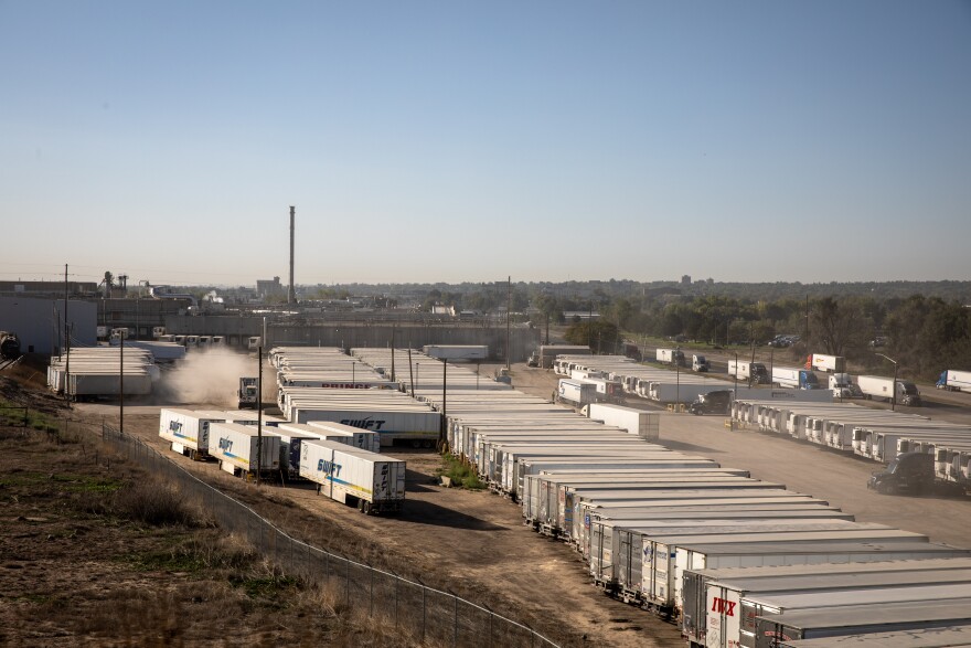 This photo taken outside the JBS meatpacking plant in Greeley, shows dozens of large semi trucks in a dirt parking lot. Some of the trucks read "Swift" on the side.