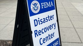 A blue and white FEMA disaster recovery center sign on a sidewalk outside a building