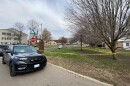 Crime scene tape along several homes and apartment buildings in an urban neighborhood with a police car parked at the curb