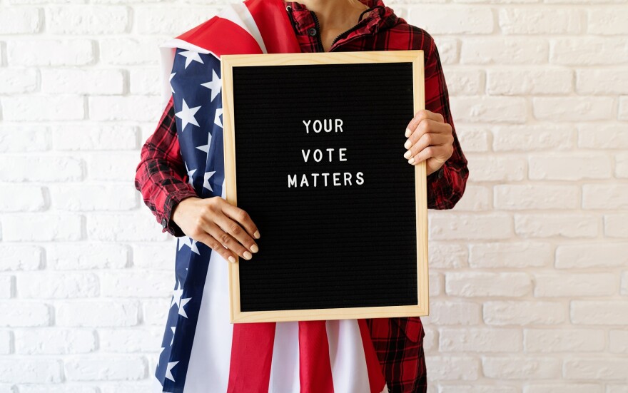 Woman with american flag holding letter board with text Your Vote Matters on white brick background