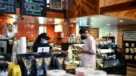 A picture of a masked barista helping a maksed customer in a California coffee shop.