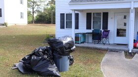 A pile of trash bags on the front lawn of a white townhouse. 