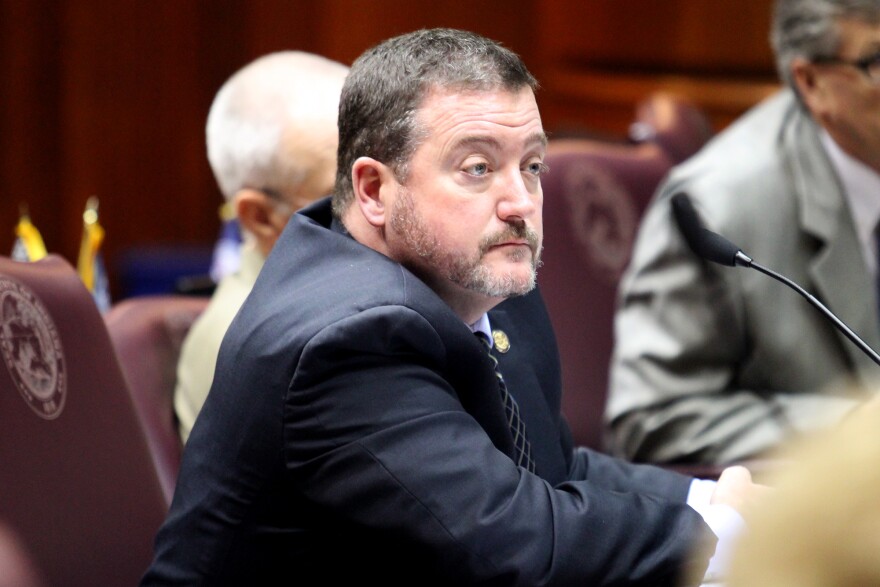 Indiana Republican Representative Chuck Goodrich sits at his desk on the House floor. Goodrich is a White man with dark, graying hair and beard.