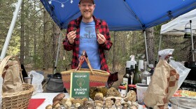 Dr. Gordon Walker poses behind a table of mushrooms and his book “Passport to Kingdom Fungi” near Mount Shasta, California in May 2025.