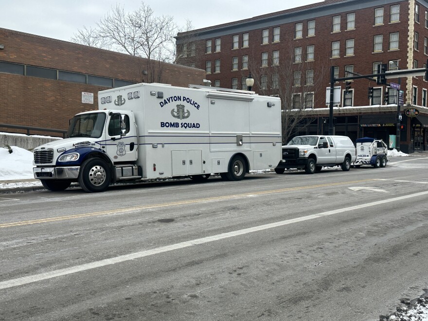 A white police bomb squad truck parked on a street in front of a brick building. Snow is on the ground.