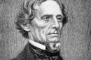 A black and white handdrawn portrait  of a man with short wavy hair and a chin beard in a black suit with white, high-collar shirt and black cravat. 