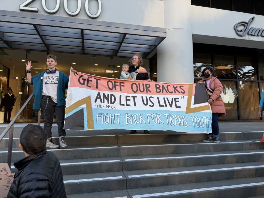 Organizers with Rainbow Families Action stand outside of Sutter with a sign that reads 'Get off our backs and let us live' 'fight back for trans youth'