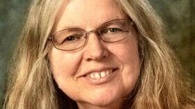 A woman with shoulder-length sandy colored hair and glasses smiles for the camera.