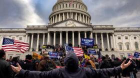 A crowd of people with American flags and Trump signs stand in front of the capitol.