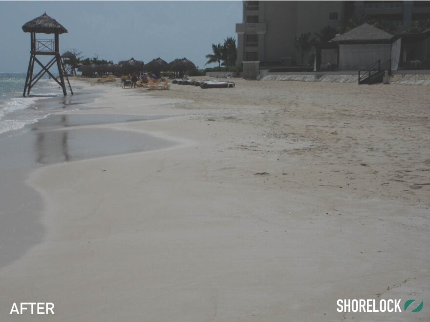 A beach with sand in the foreground, a lifeguard station, and building in the background