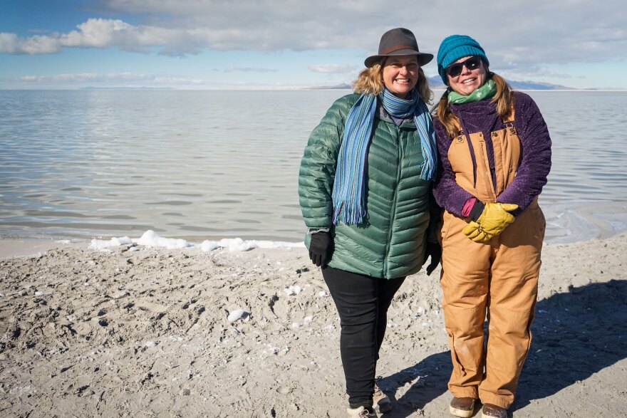 Poet Nan Seymour, left, and biologist Jaimi Butler stand in front of some white, fluffy foam on the shoreline of the Great Salt Lake.