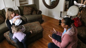 Doula Janice Ingram (right corner) talks to Anna Ferguson at a postpartum visit as Ferguson's toddler tries to climb onto her lap. Ferguson had experienced some complications following the birth of her youngest daughter and Ingram was there to check in on her.