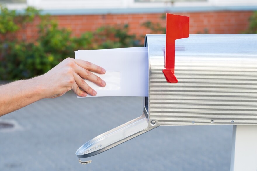 Close-up of a hand and forearm putting mail in a mailbox