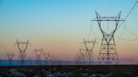 The silhouette of a power transmission line vanishing into a point in the distance during sunset.