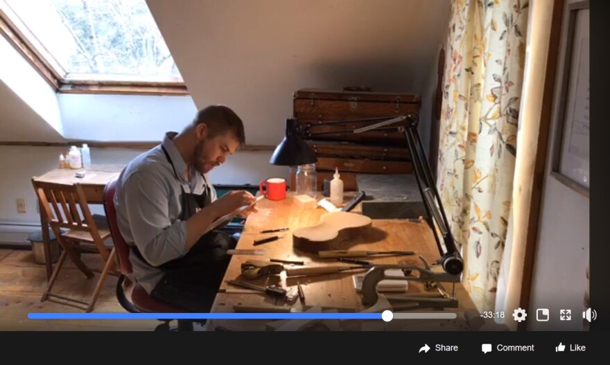 A screenshot of a Facebook live video of someone in an apron looking over the pieces of a violin.