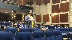 A woman in a face mask speaks into a mic inside the Alamo Heights High School auditorium.