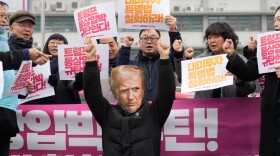 A South Korean protester, wearing a mask of U.S. President Donald Trump, gestures during a rally against Trump's tariffs policy on South Korea, near the U.S. embassy in Seoul, South Korea, Wednesday, Feb. 11, 2026. The banners, in red, read "We condemn Trump's trade pressure." (AP Photo/Ahn Young-joon)