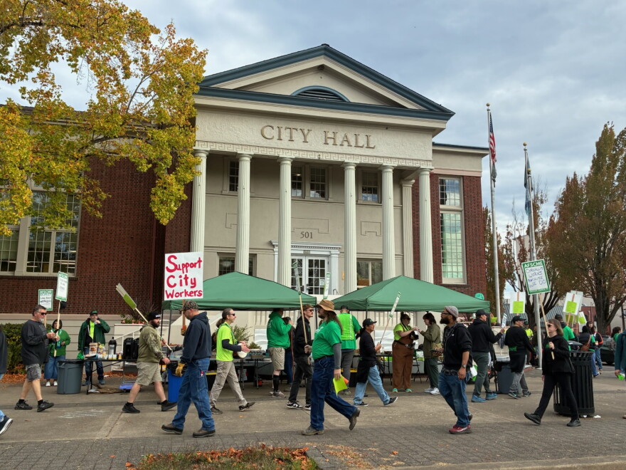 A group of people holding picket signs on a sidewalk in front of the Corvallis City Hall.