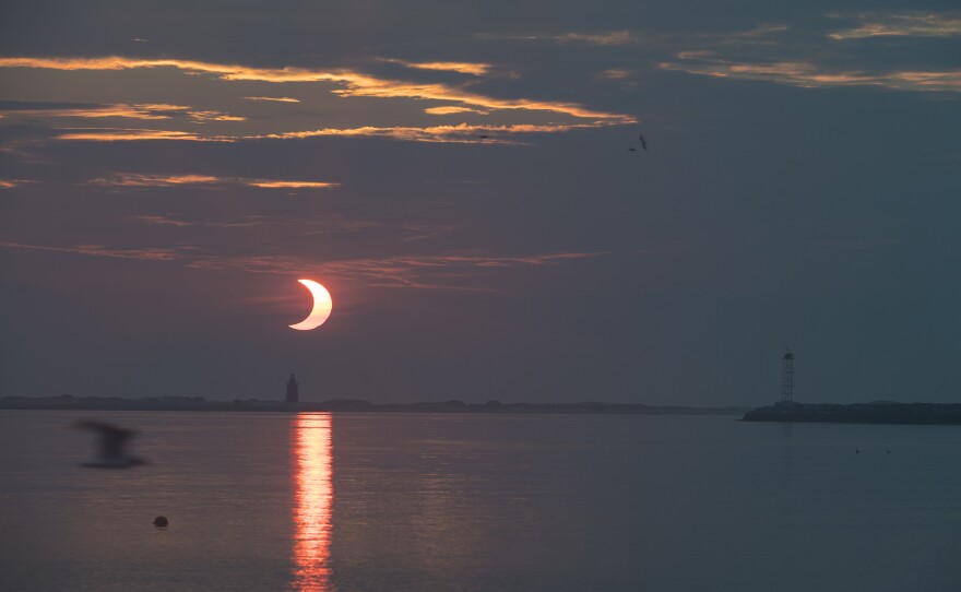 In this image provided by NASA, a partial solar eclipse is seen as the sun rises behind the Delaware Breakwater Lighthouse in Lewes, Del.