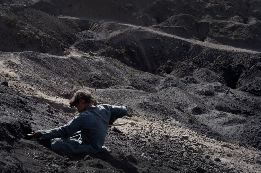Mansour plays in the dirt on the edge of the mountain where the mine entrance is located.