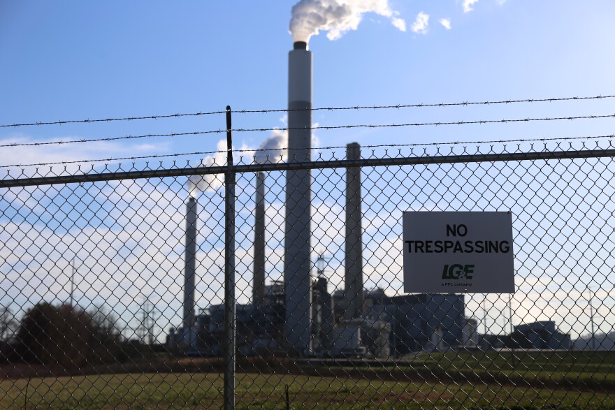 Smoke stacks behind chain link fence with "no trespassing sign." Blue sky background.