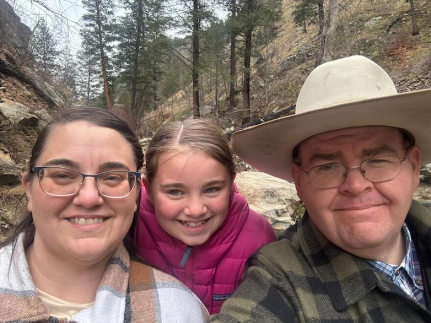 Tara Benson, Grace Benson and Jake Benson are framed together in a family photo with a mountainous background with green trees. 
