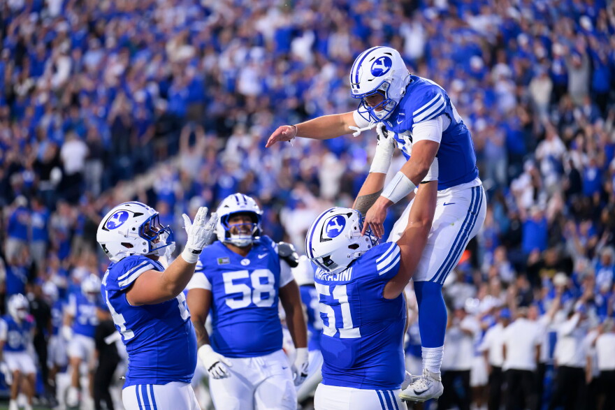 BYU offensive lineman Sonny Makasini, center right, lifts quarterback Bear Bachmeier, top, after Bachmeier ran for a touchdown during the first half of an NCAA college football game against Notre Dame, Saturday, Oct. 17, 2026, in Provo, Utah.