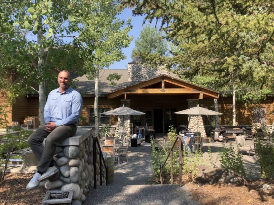 A man sits on a rock wall in front of communal grilling areas.