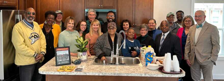 large group of people posing and smiling around a kitchen island