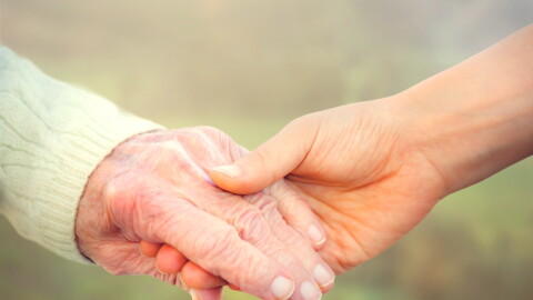 Elderly woman holding hands with young caretaker
