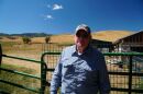 Dick Tennant at his Morgan farm with his goats grazing behind him.