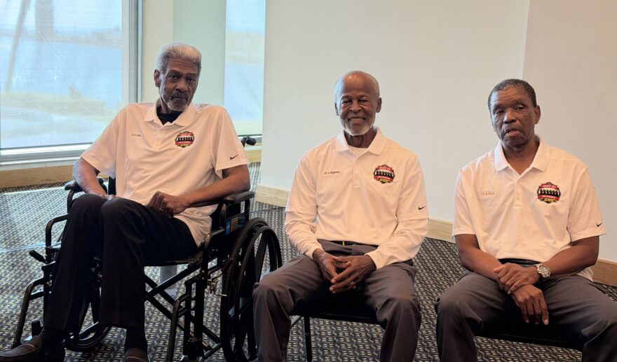Three older African American men wearing white tshirts sitting down 
