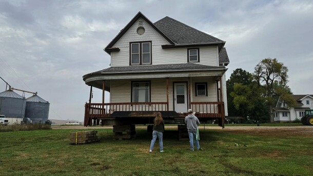 A man and woman have their backs to the camera. They are looking up at a home that is sitting on top of slabs of wood.
