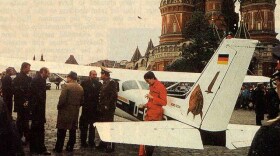 Mathias Rust leans against his Cessna in Red Square, while Soviet officials stand around in a group nearby