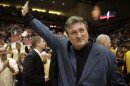 man waves to the crowd during a tribute. there are arena stands and fans in the background