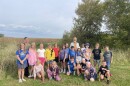 John Latimer, Michelle Martin, and about 20 elementary school students stand near a field and forest.