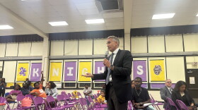An image of Norfolk Public Schools Superintendent Jeff Rose standing in the cafetorium of P.B. Young Elementary holding a microphone while answering questions about a school consolidation plan. 