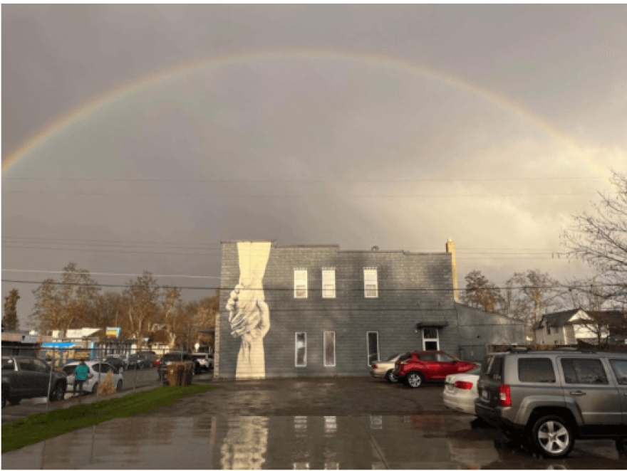 A building in the rain with a picture of two hands clasping painted on its side.