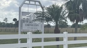 A white fence and a white sign that says "Howard Cattle Corporation."